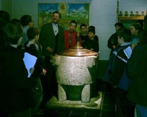 Dechant Vilz † umringt mit den interessierten Schülern das frühromanische Taufbecken.
